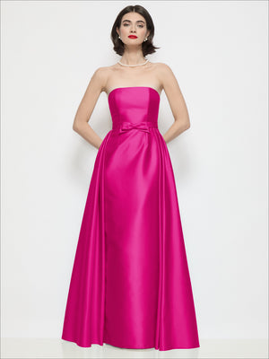 Fuchsia pink strapless satin column dress with waist bow and draped overskirt, front